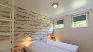 Un dormitorio con cama, dos ventanas, pared de madera y una lámpara en el techo.