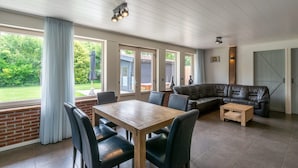 Un salón amplio con una mesa de comedor de madera, un sofá de cuero y ventanas grandes que ofrecen vistas al exterior.