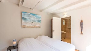 Ein Schlafzimmer mit einem Bett, einem Strandbild, einer Lampe und einem durchgegangenen Tür sichtbaren Badezimmer.