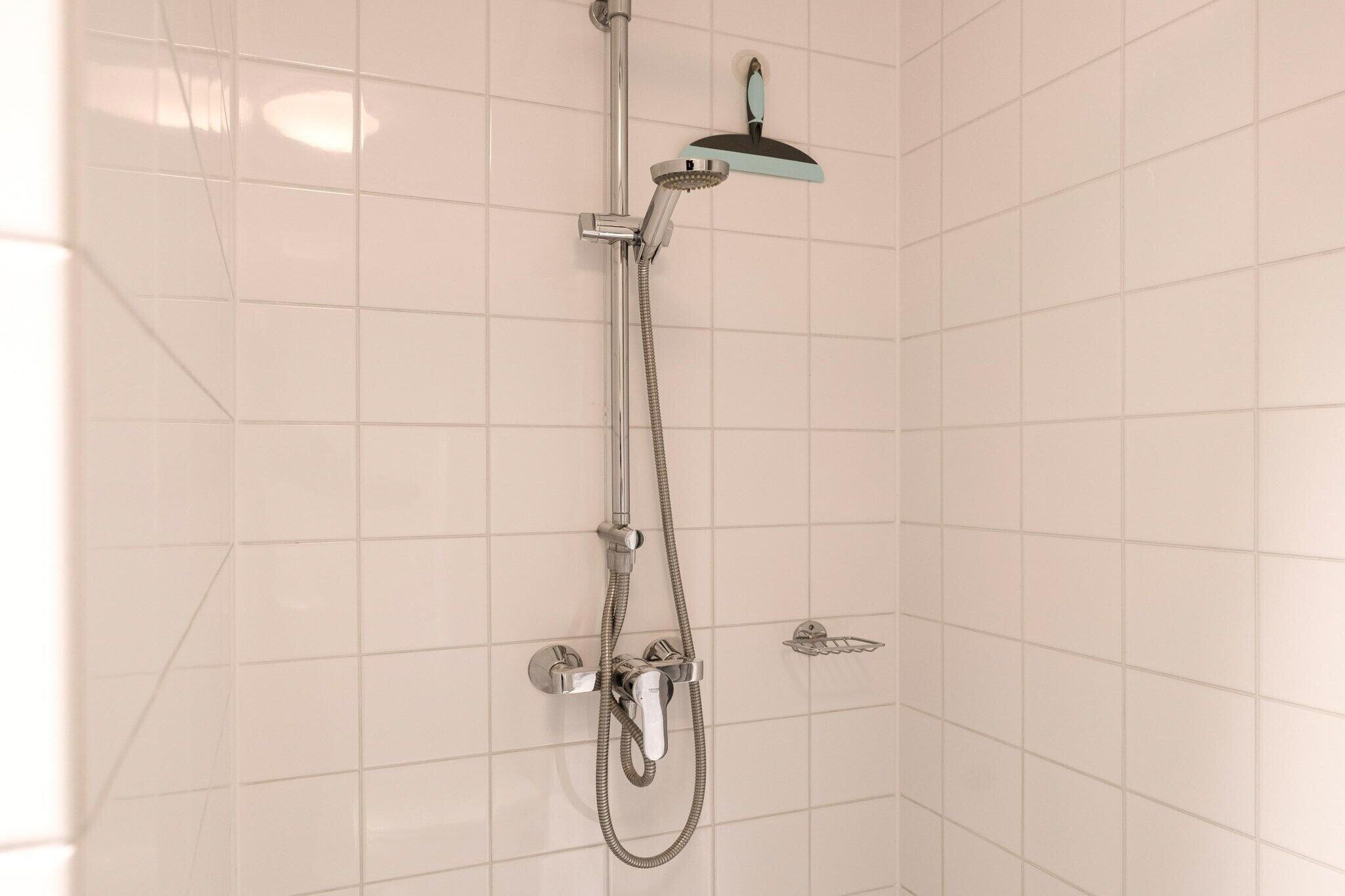 Eine Dusche mit Handbrause und am Wand montiertem Wasserhahn.