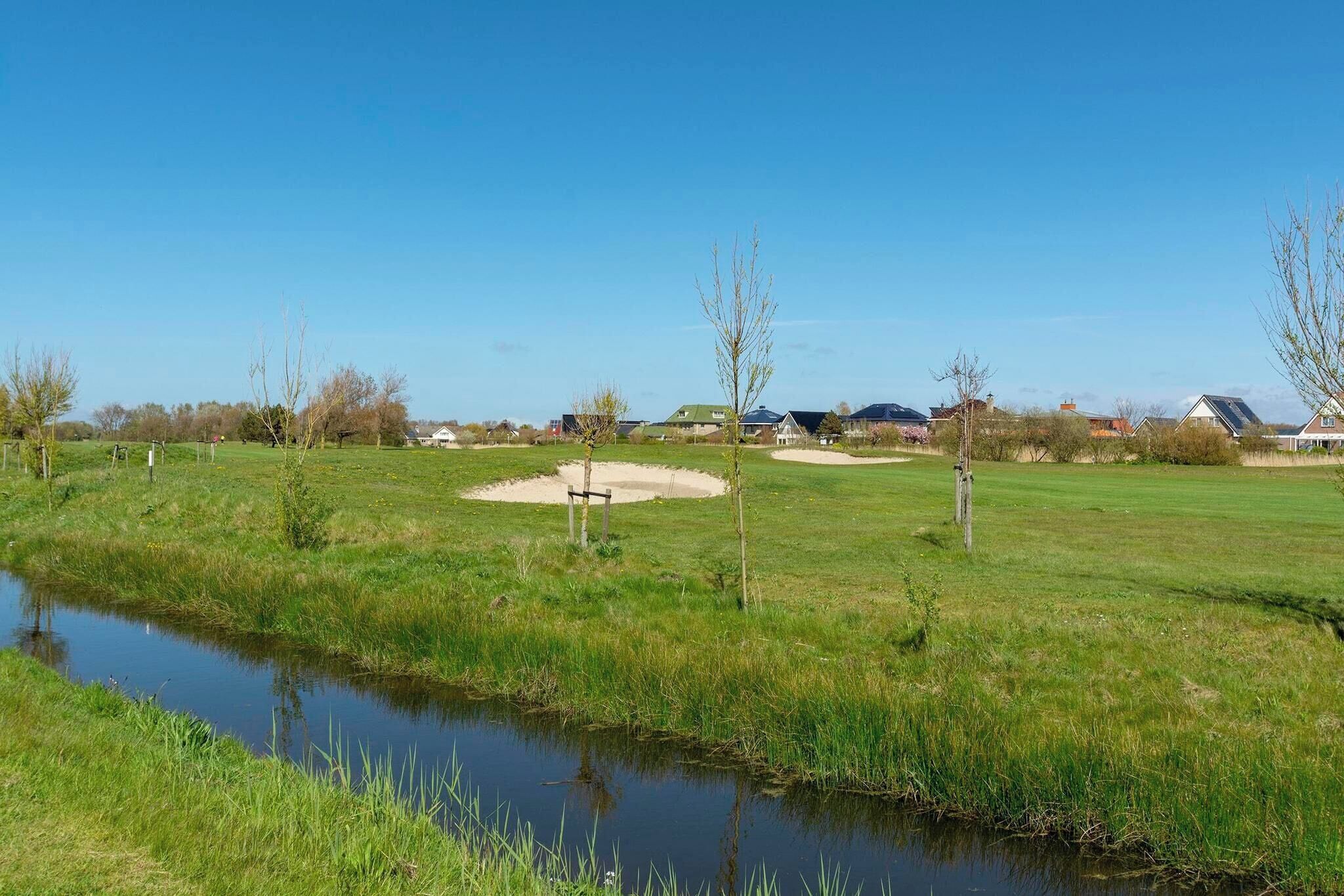 A golf course with a pond, sand bunkers, and sparse trees.