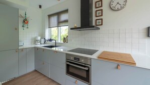 A modern kitchen with a built-in oven, a black range hood, and a clock on the wall. - De Zeester 4-person holiday home n De Koog (Callantsoog)
