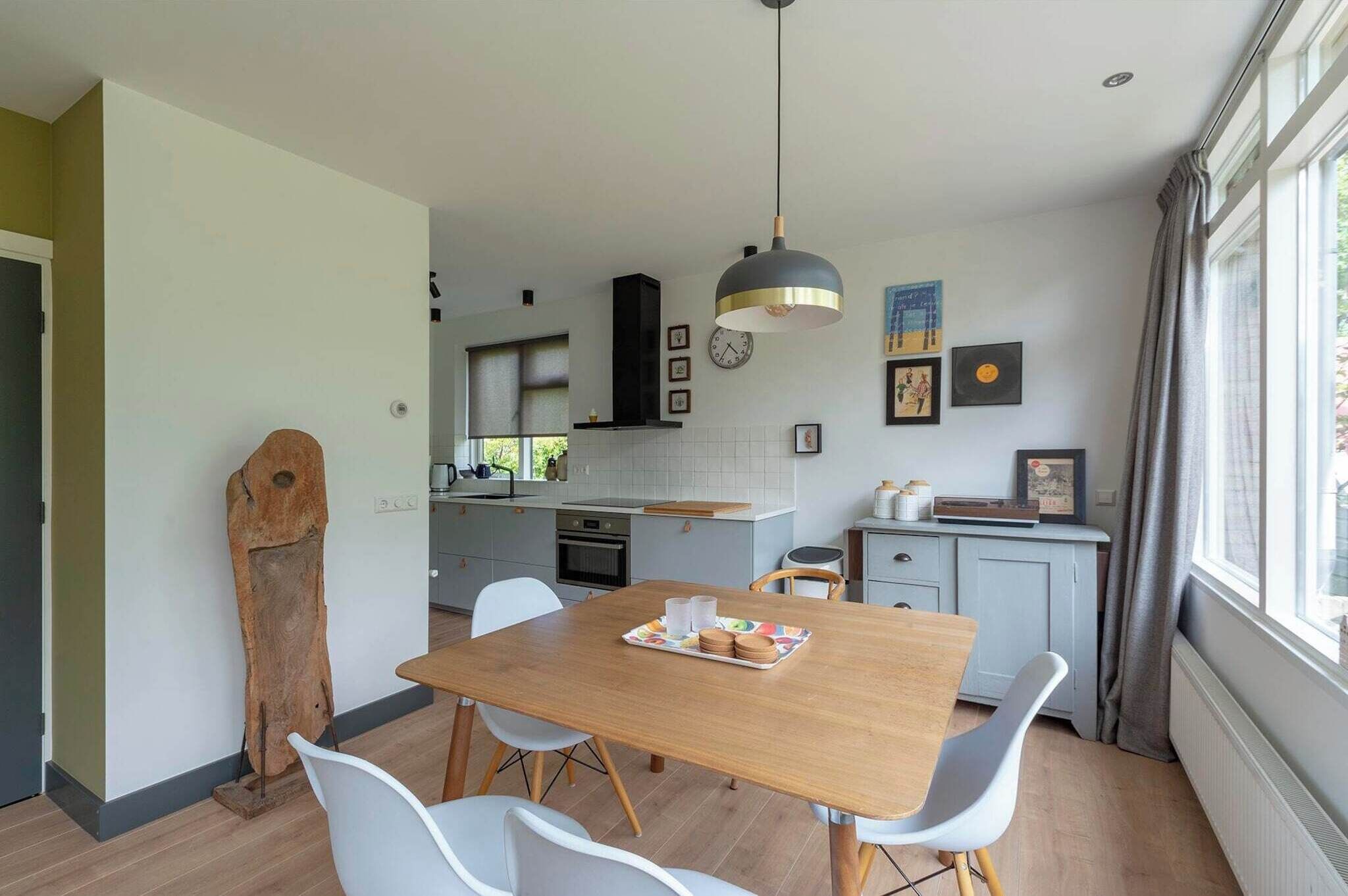 A modern kitchen with a wooden dining table, white chairs, and a pendant light.