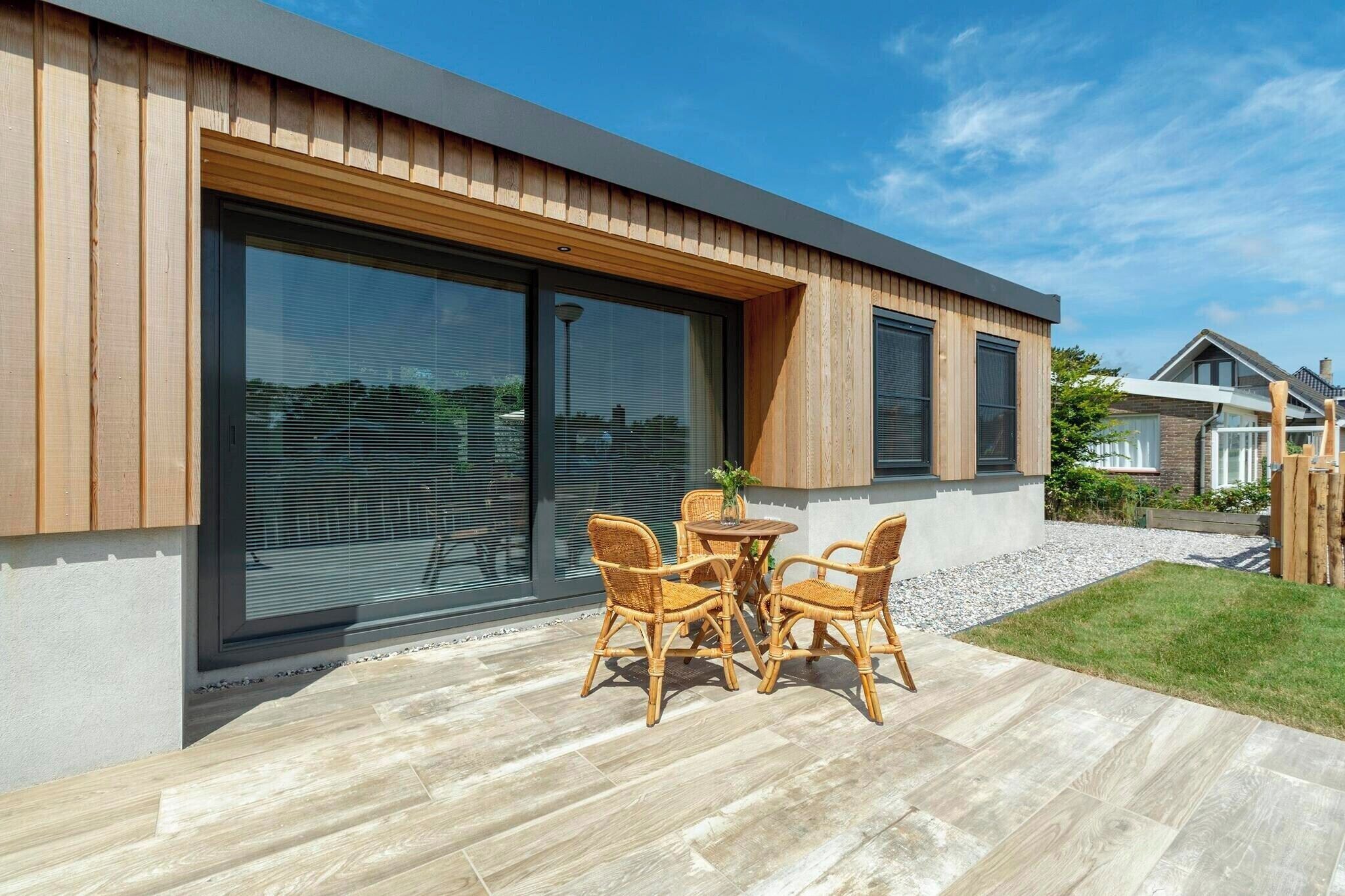 Une maison moderne dotée de grandes portes-fenêtres coulissantes, d’une terrasse avec une table et des chaises, et d’une pelouse bien entretenue.