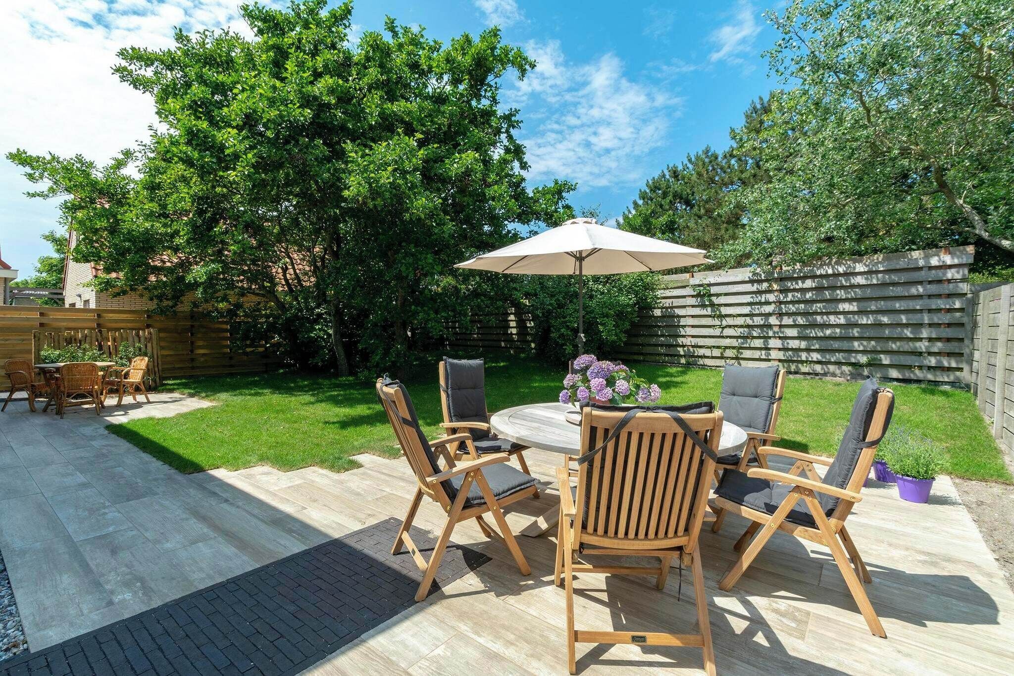 An outdoor patio with a round table and four chairs, surrounded by a wooden fence and lush greenery.