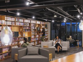 Una biblioteca moderna con estanterías, asientos cómodos y una persona leyendo.
