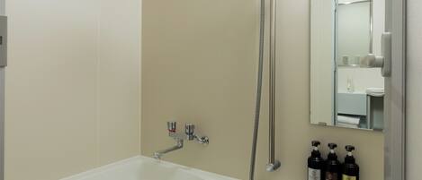 A bathroom with a bathtub, a shower, and a shelf with toiletries.
