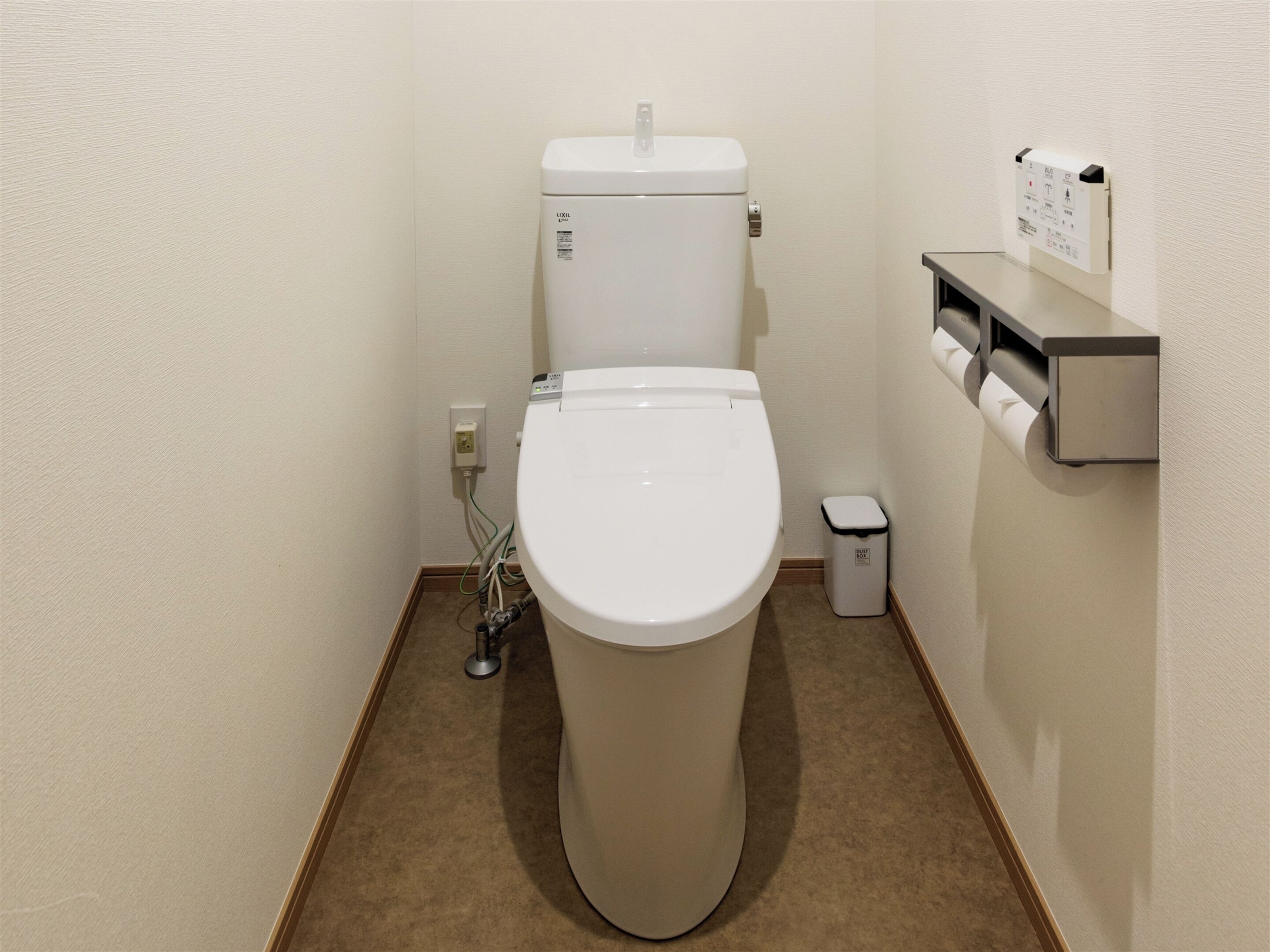 Un baño compacto con inodoro blanco, un pequeño cesto de basura y dispensador de papel de pared.