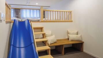A child-friendly room with a blue slide, wooden steps, and a small bench with pillows.