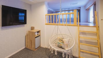 A room with a TV mounted on the wall, a wooden cabinet, a hanging chair, a ladder, and a bunk bed with a wooden railing.