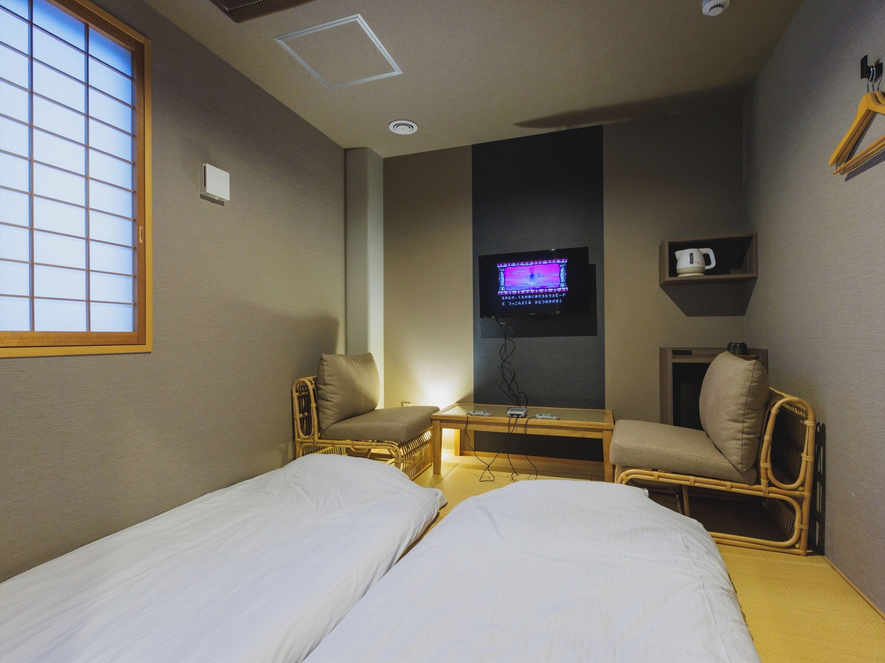 A small hotel room with two single beds, a television, a small table, and a window with a view.