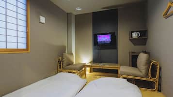 A small hotel room with two single beds, a television, a small table, and a window with a view.