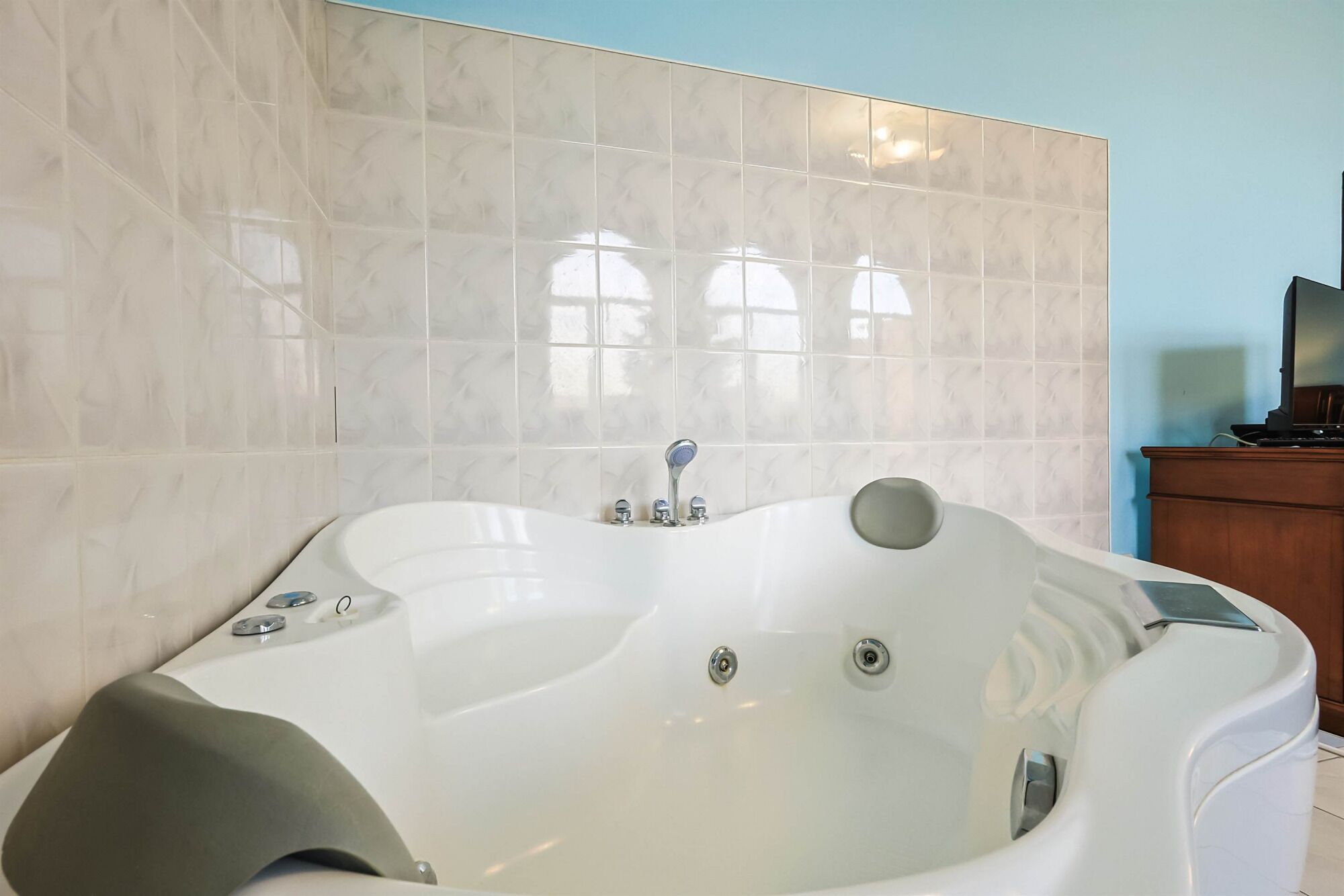 Un baño moderno con una bañera blanca grande, un armario de madera y un revestimiento de baldosas.