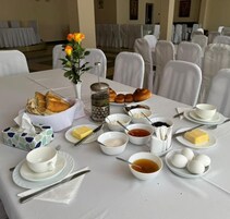 Una mesa de desayuno servida con pan, huevos, mantequilla y diferentes aderezos.