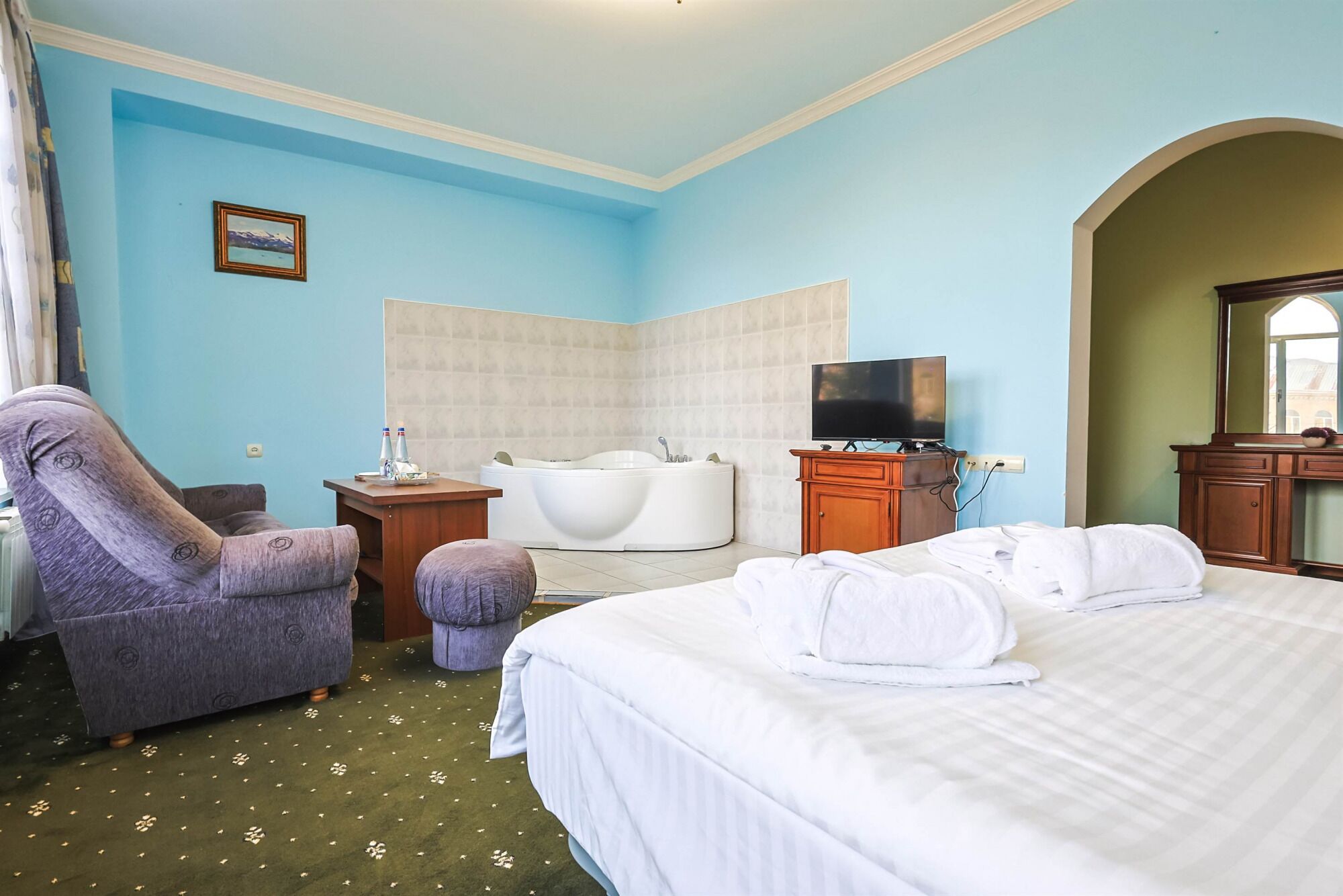 Una habitación de hotel con cama, una silla, una bañera, televisión y escritorio.