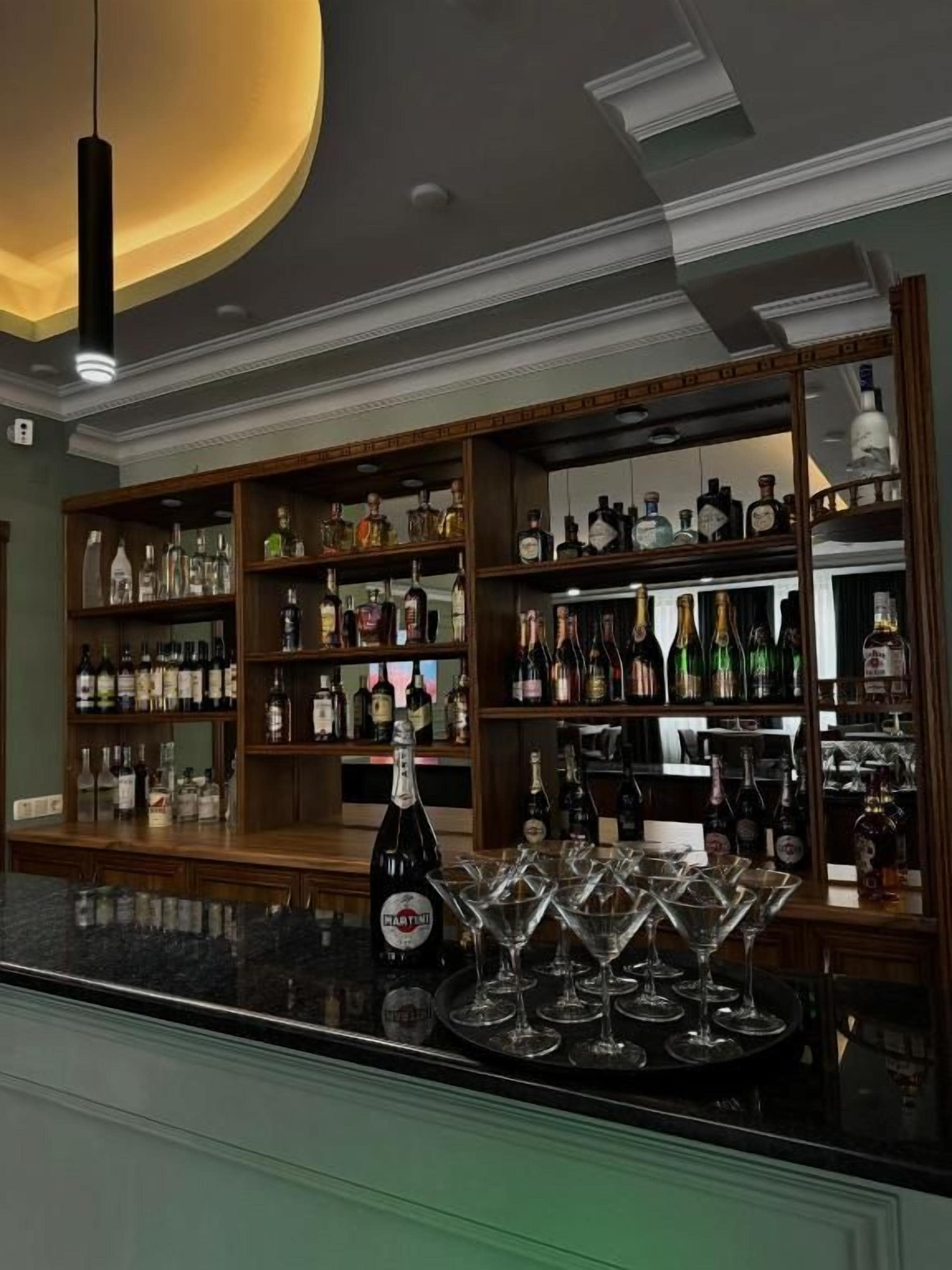 A bar area with shelves of liquor bottles, a bottle of Martini, and several martini glasses on the counter.