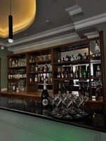 Zona de bar con estantes llenos de botellas de licor, una botella de Martini y varios vasos de martini sobre la barra.