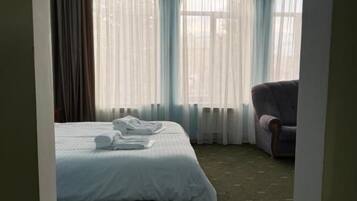 Una habitación de hotel con cama, una silla y ventanas grandes con cortinas.