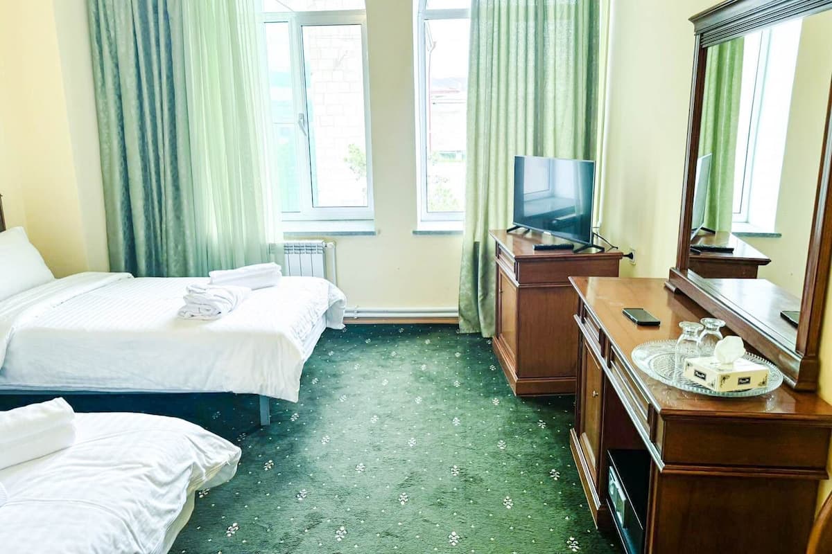 A hotel room with two beds, a television, a dresser, and a mirror.