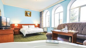 A hotel room with a bed, a sofa, a table with a bottle and cups, a TV, and a painting on the wall. - Lalaner Hotel (Sisian)