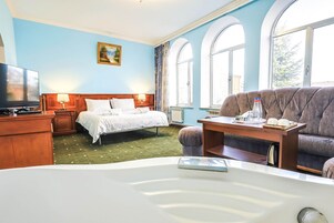 Una habitación de hotel con una cama, un sofá, una mesa con una botella y vasos, un televisor y un cuadro en la pared.