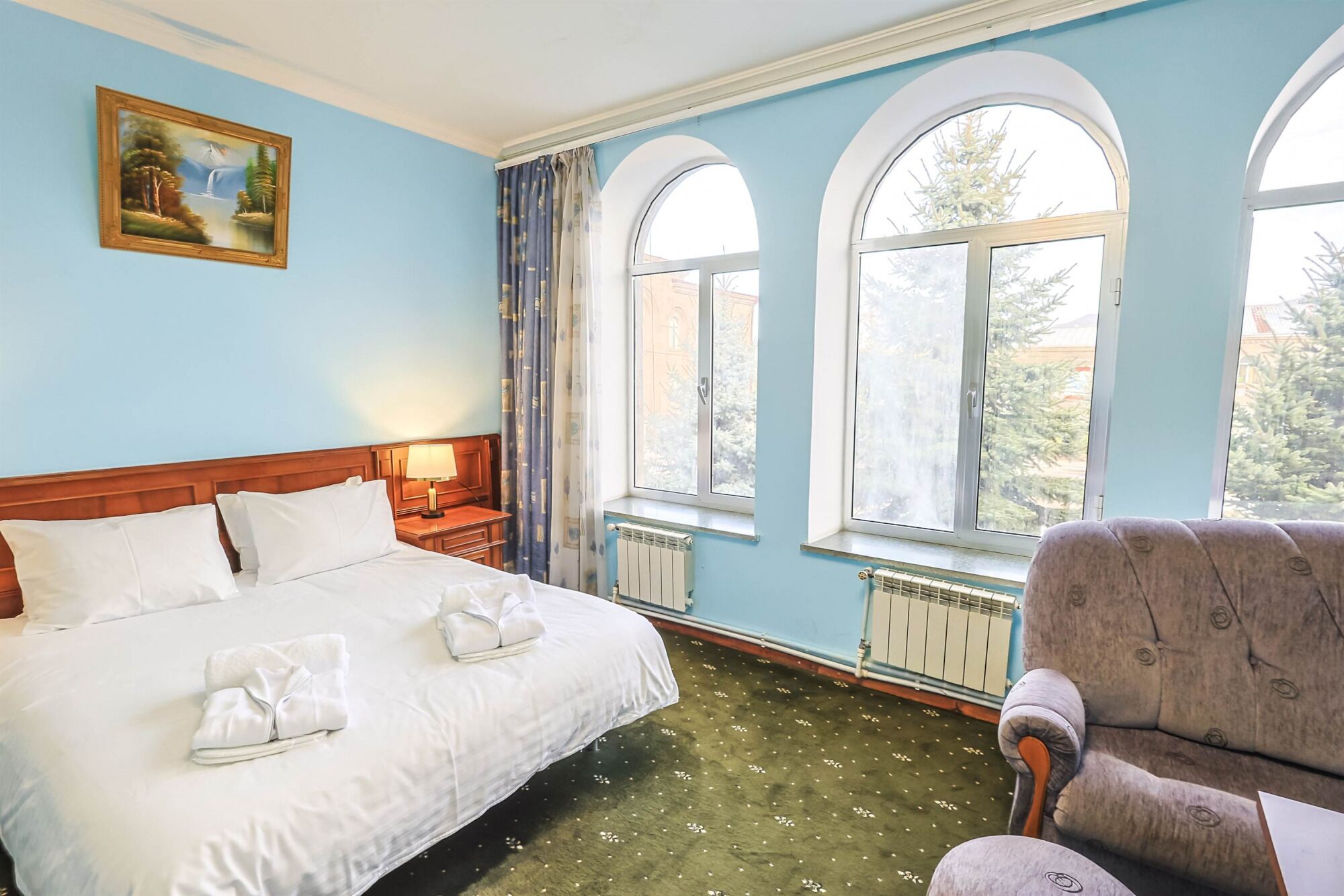 A hotel room with a large bed, a chair, and two windows with arched tops.