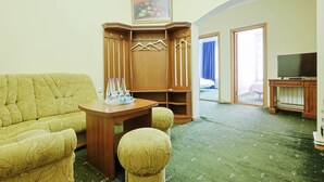 A hotel room with a green carpet, a sofa, a wooden cabinet with hanging clothes, a television, and a painting on the wall. - Lalaner Hotel (Sisian)