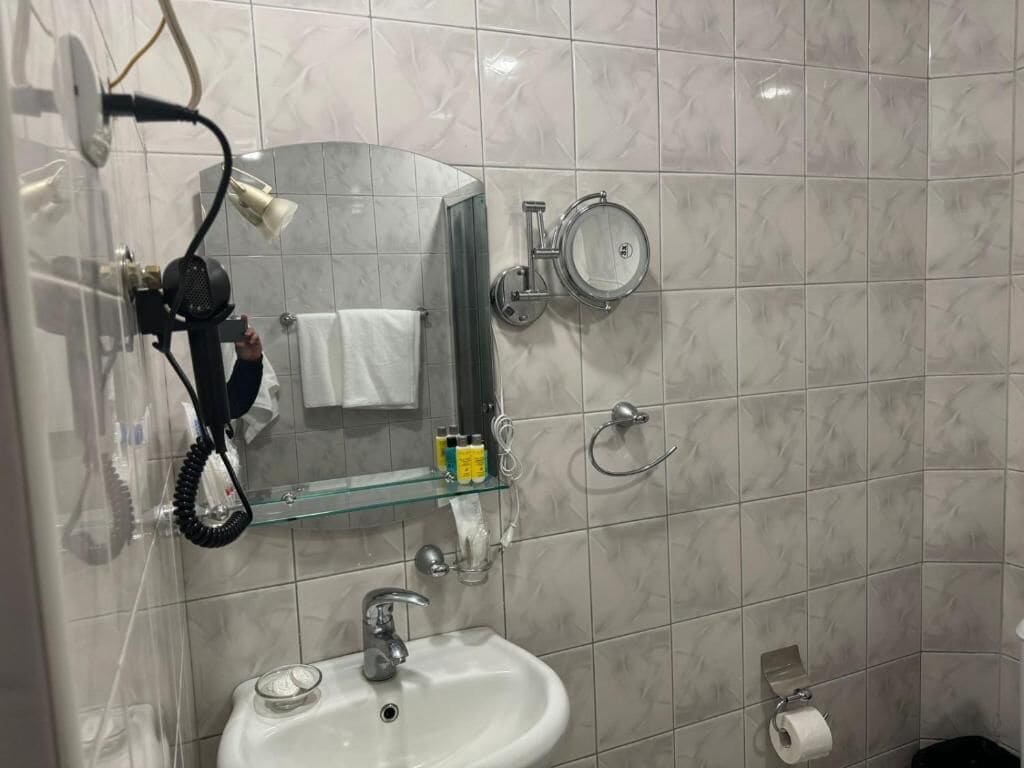 A bathroom with a glass shower enclosure, a white sink, and a towel rack.