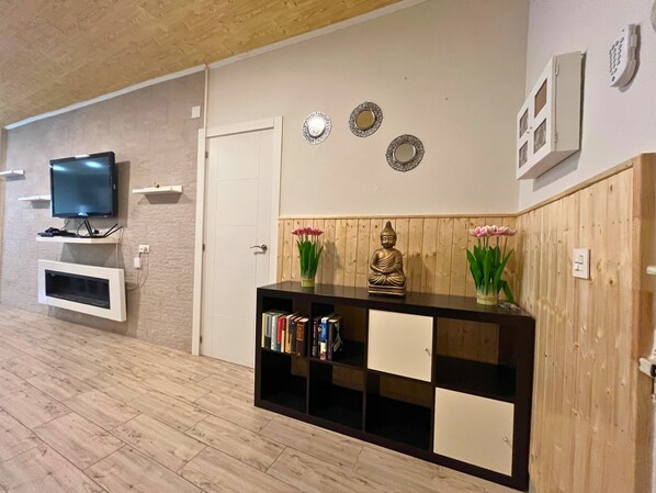 Una sala moderna con un televisor de pantalla plana montado en la pared, una mesa consola de madera con libros y objetos decorativos, y una puerta con marco blanco.