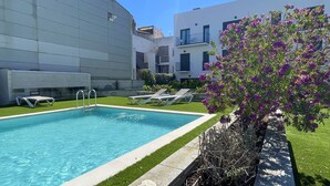 Une piscine rectangulaire à l’eau d’un bleu cristallin, entourée d’une pelouse bien entretenue et bordée d’une rangée de chaises longues.