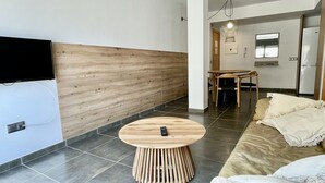 Une chambre d’hôtel moderne avec un mur d’accent en bois, une table ronde en bois, un canapé et un téléviseur fixé au mur.