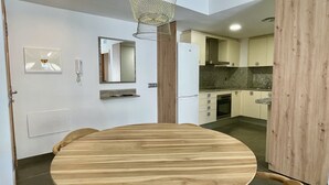 Une cuisine moderne avec une table à manger en bois, un luminaire suspendu et un réfrigérateur.