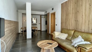 Un salon moderne avec un canapé, une table basse ronde en bois et un téléviseur fixé au mur.
