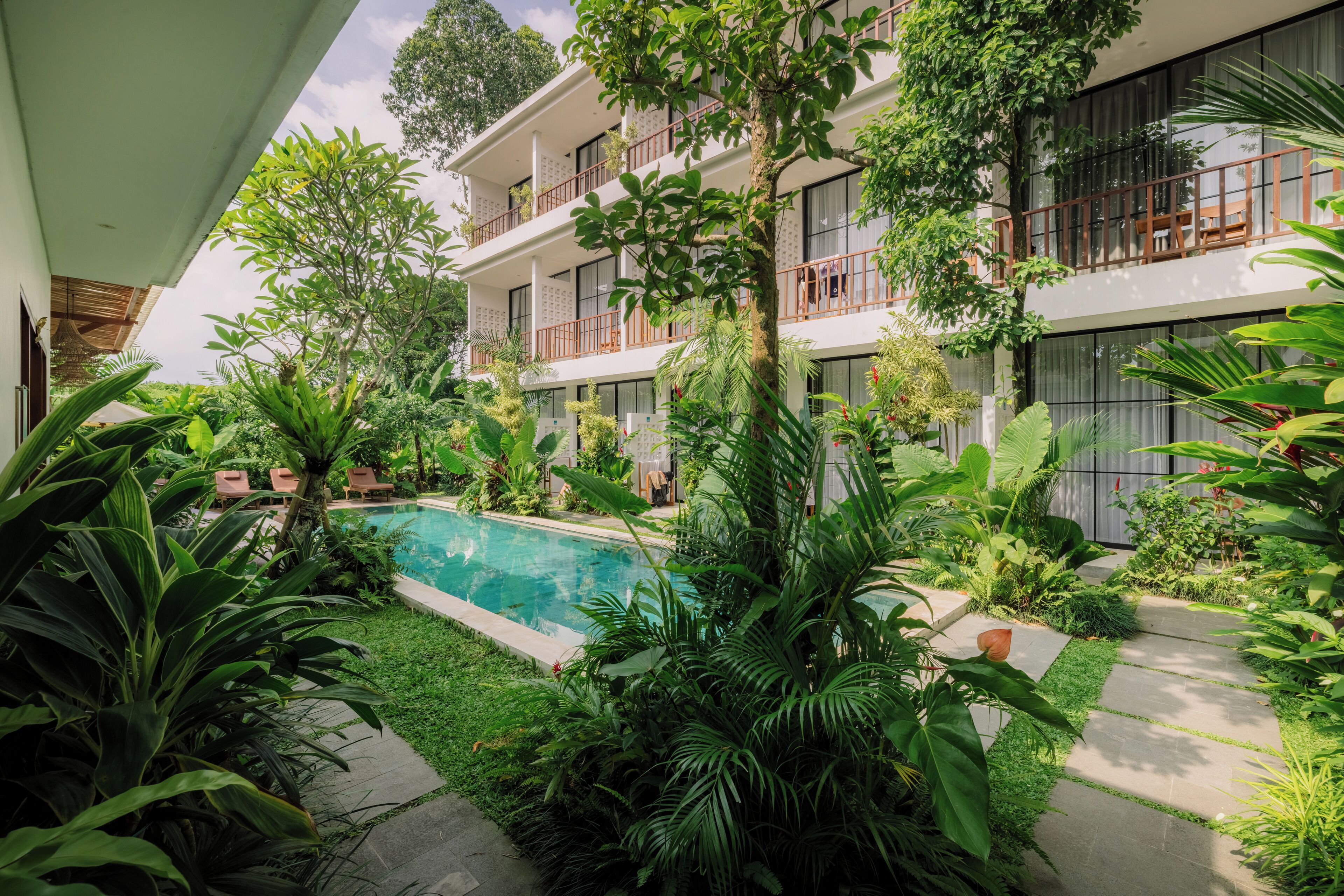 A modern hotel with a pool surrounded by lush greenery and a two-story building with balconies.