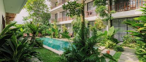 A modern hotel with a pool surrounded by lush greenery and a two-story building with balconies.