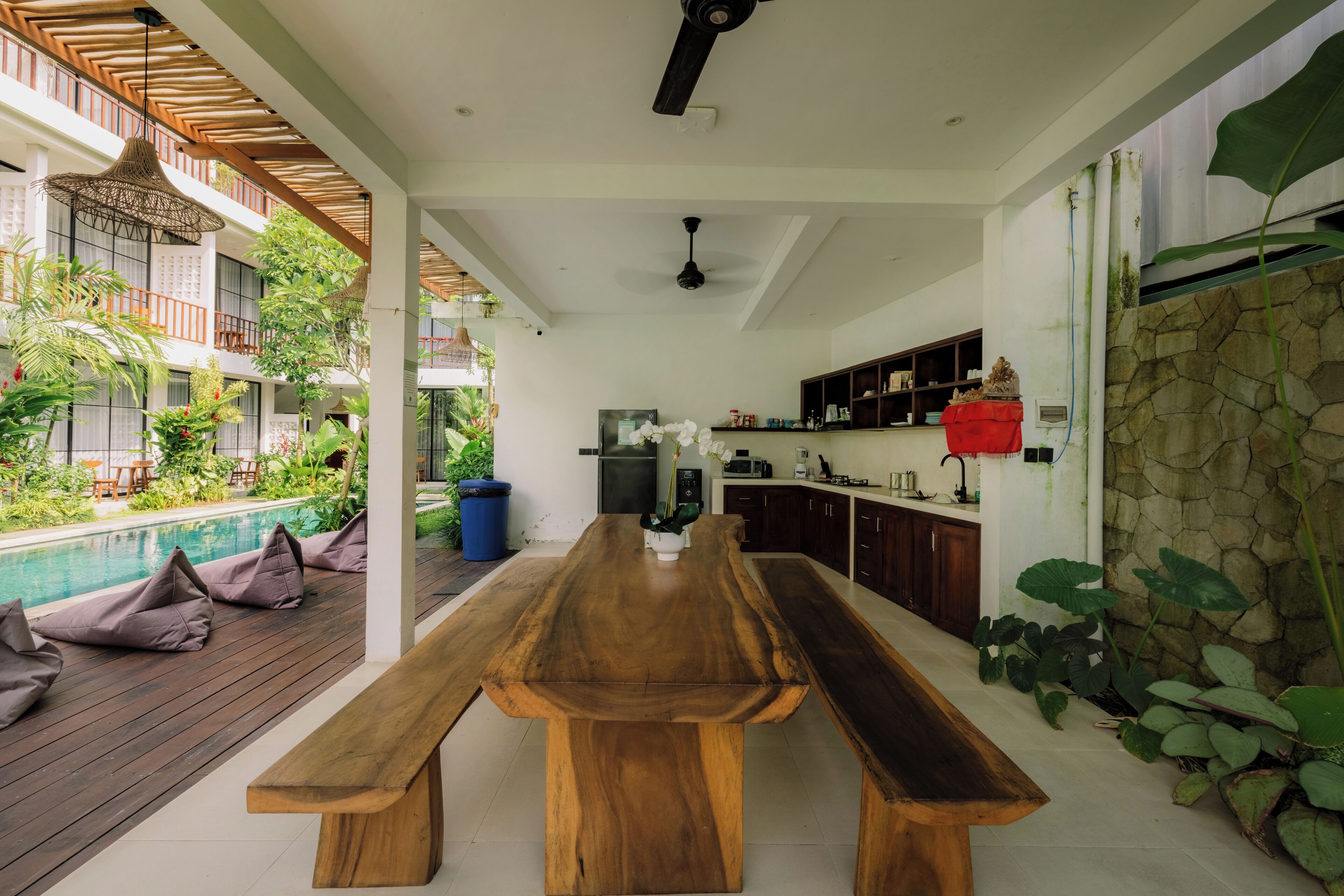 A spacious indoor area with a wooden dining table, a kitchen area, and a poolside seating area.