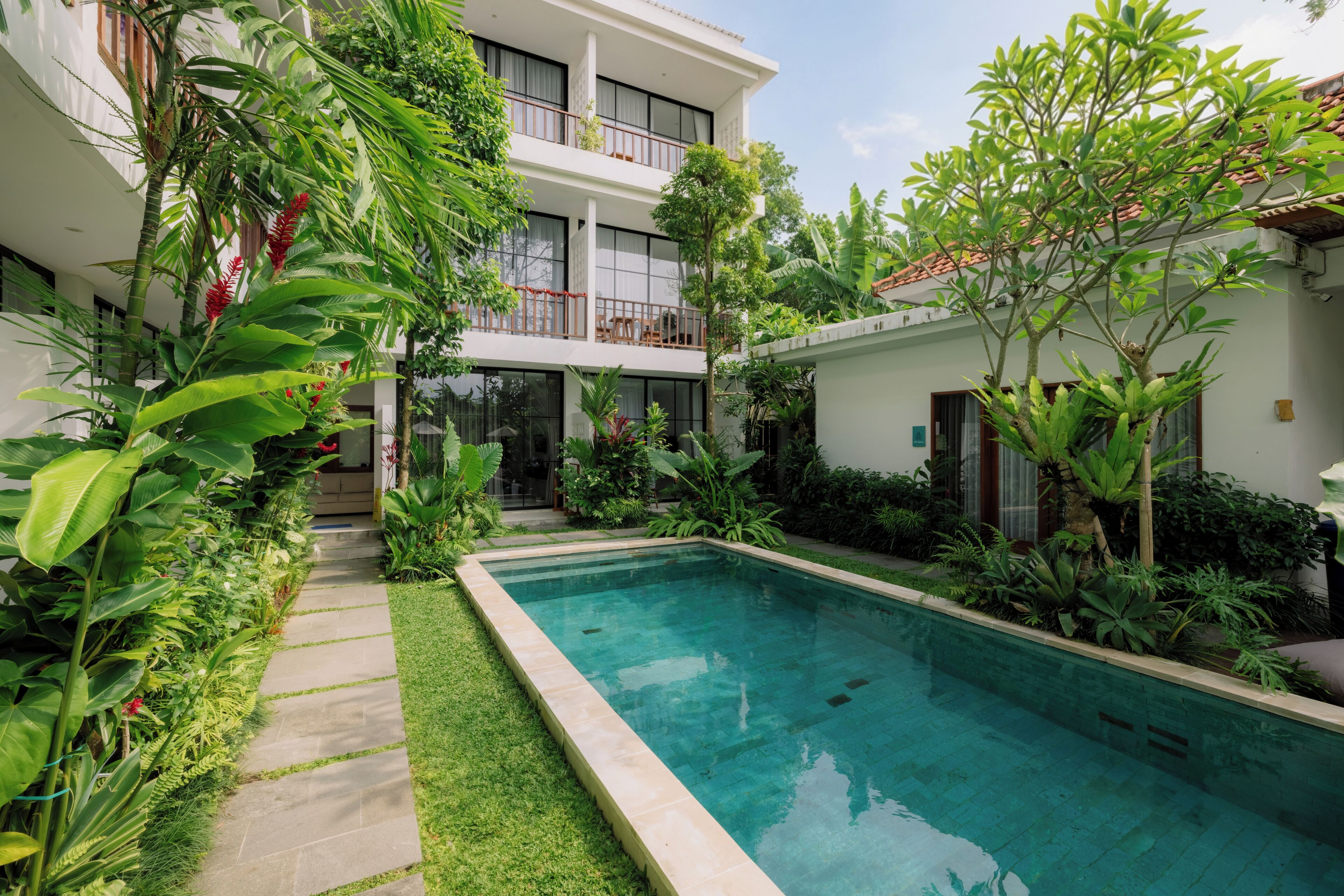 Un hôtel moderne doté d’une piscine entourée d’une végétation luxuriante et d’un bâtiment à deux étages avec des balcons.