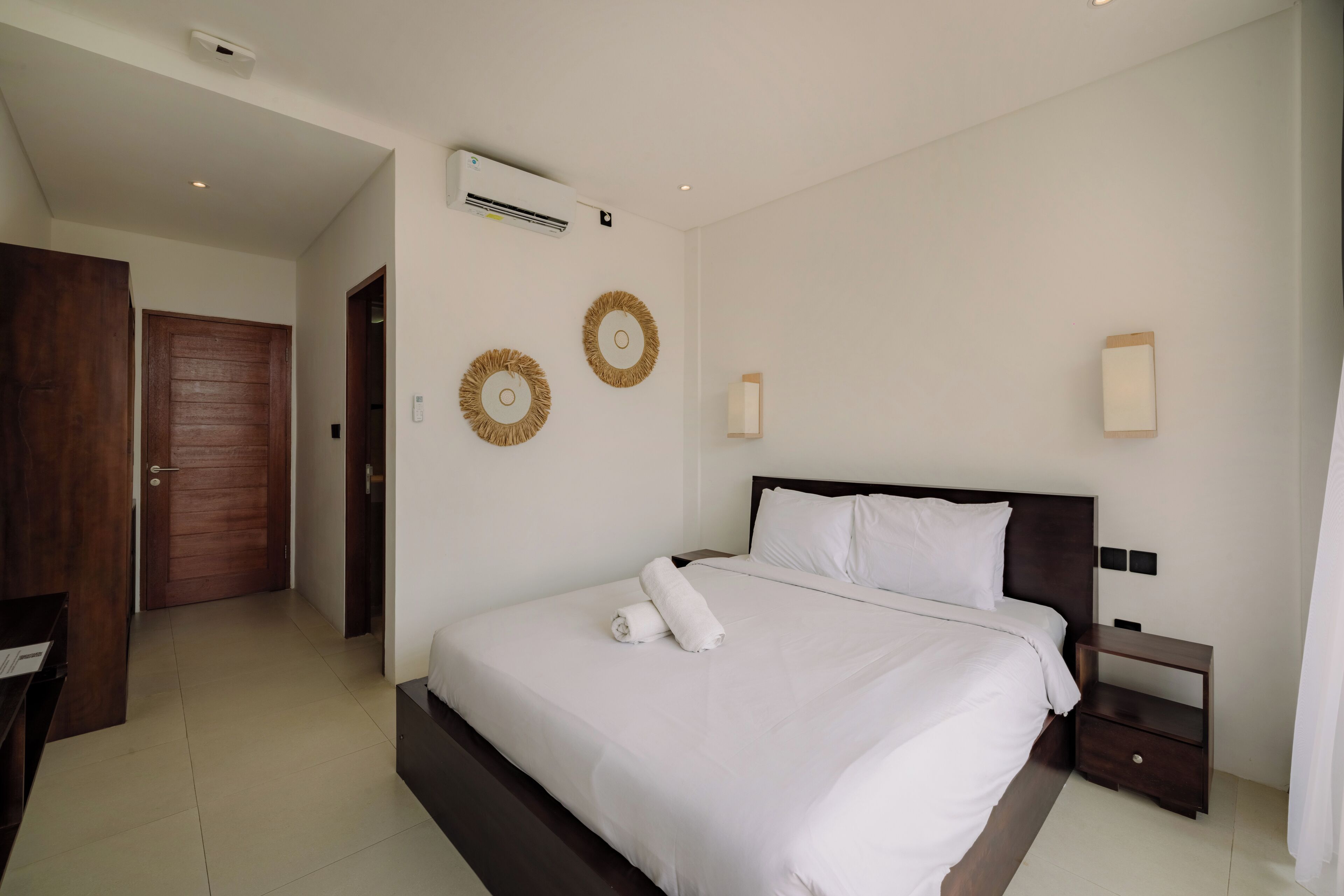 A bedroom with a large bed, a wooden door, a wall-mounted air conditioner, and two wall-mounted light fixtures.