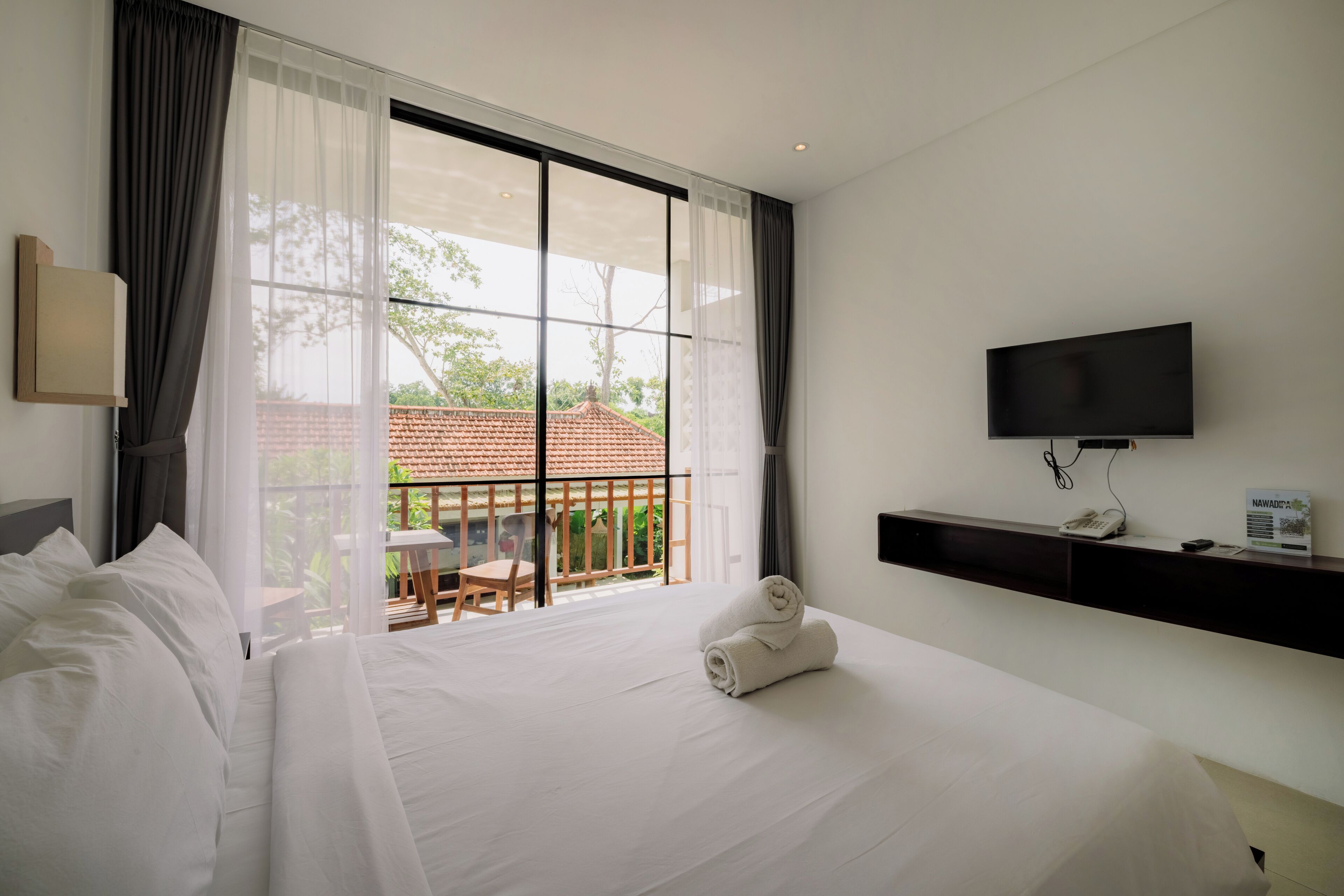 A hotel room with a large bed, a TV mounted on the wall, and a balcony with a table and chairs.