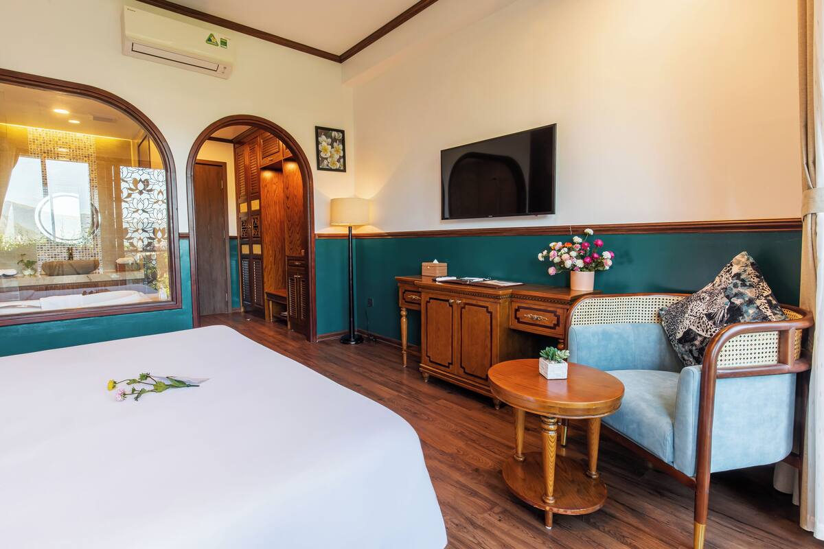 Habitación de hotel con cama, sofá, una mesita, televisor y ventana con vistas al exterior.