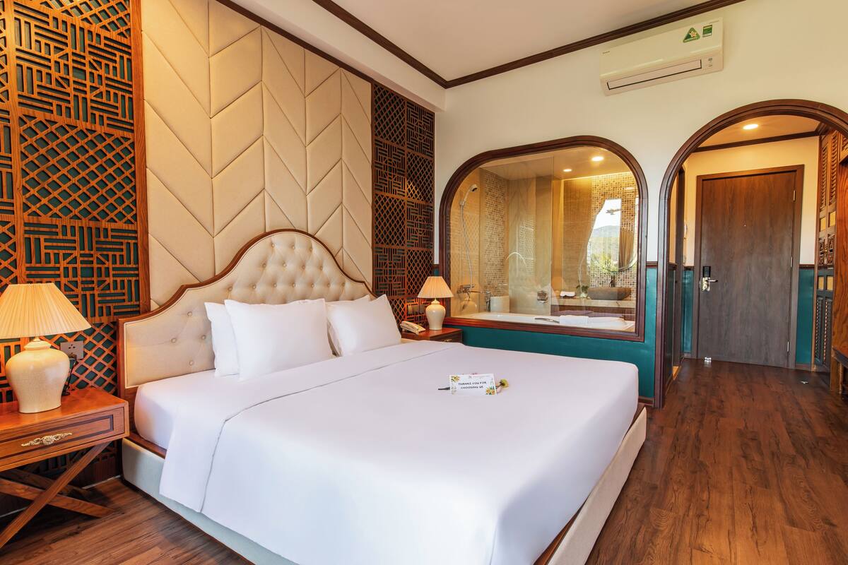 Habitación de hotel con una cama grande, dos mesitas de noche con lámparas, un espejo y suelo de madera.