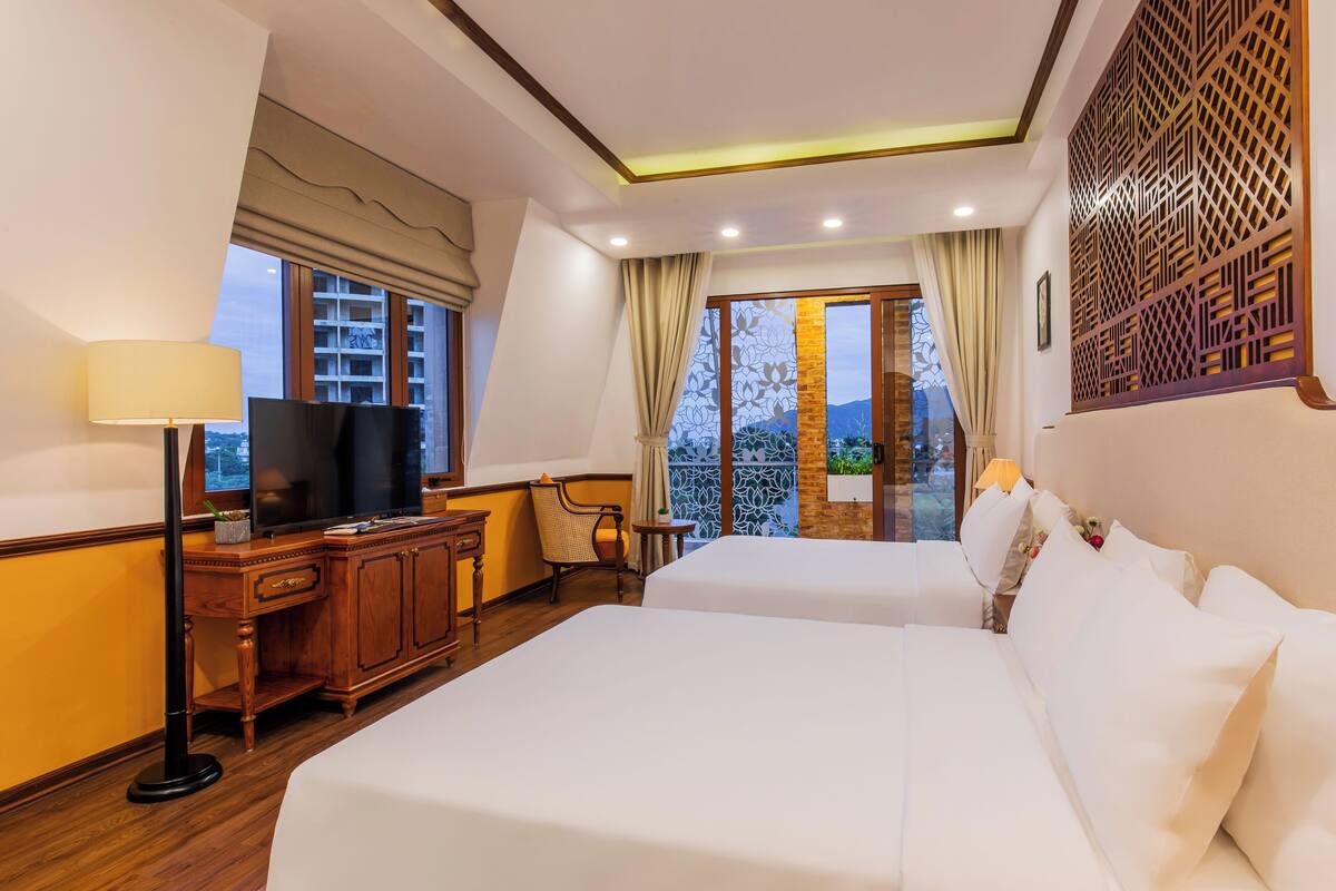 Habitación de hotel con dos camas, un escritorio con televisor y vista al exterior.