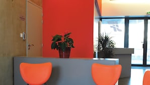 A reception area with orange chairs, a small table, and a potted plant. - jeune france accueil et formation  (Cholet)