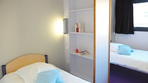 A bedroom with two beds, a wardrobe, and a window with a curtain. - jeune france accueil et formation  (Cholet)