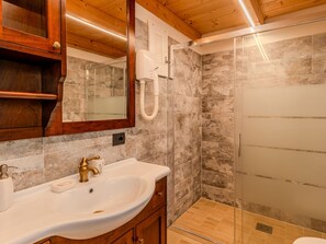 Un baño con tocador de madera, lavamanos blanco y ducha con mampara de vidrio.