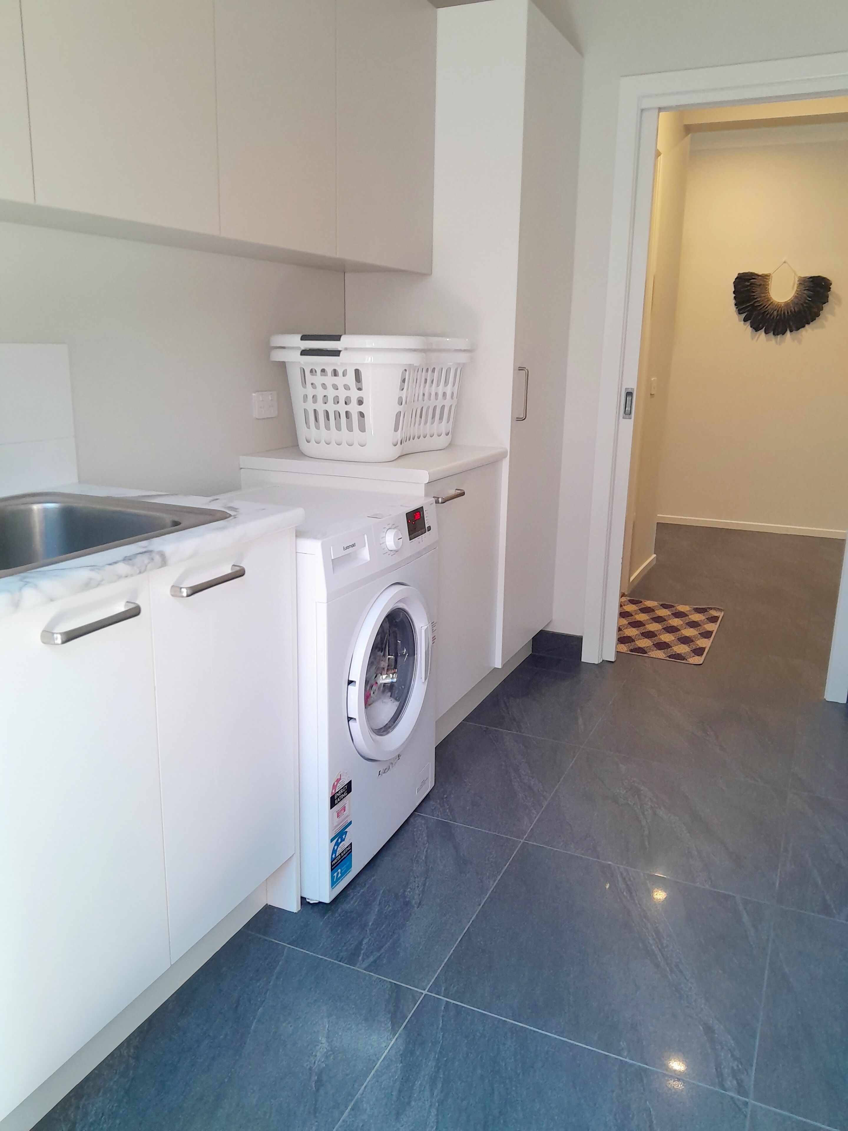 A laundry area with a washing machine, a sink, and a basket on a countertop.