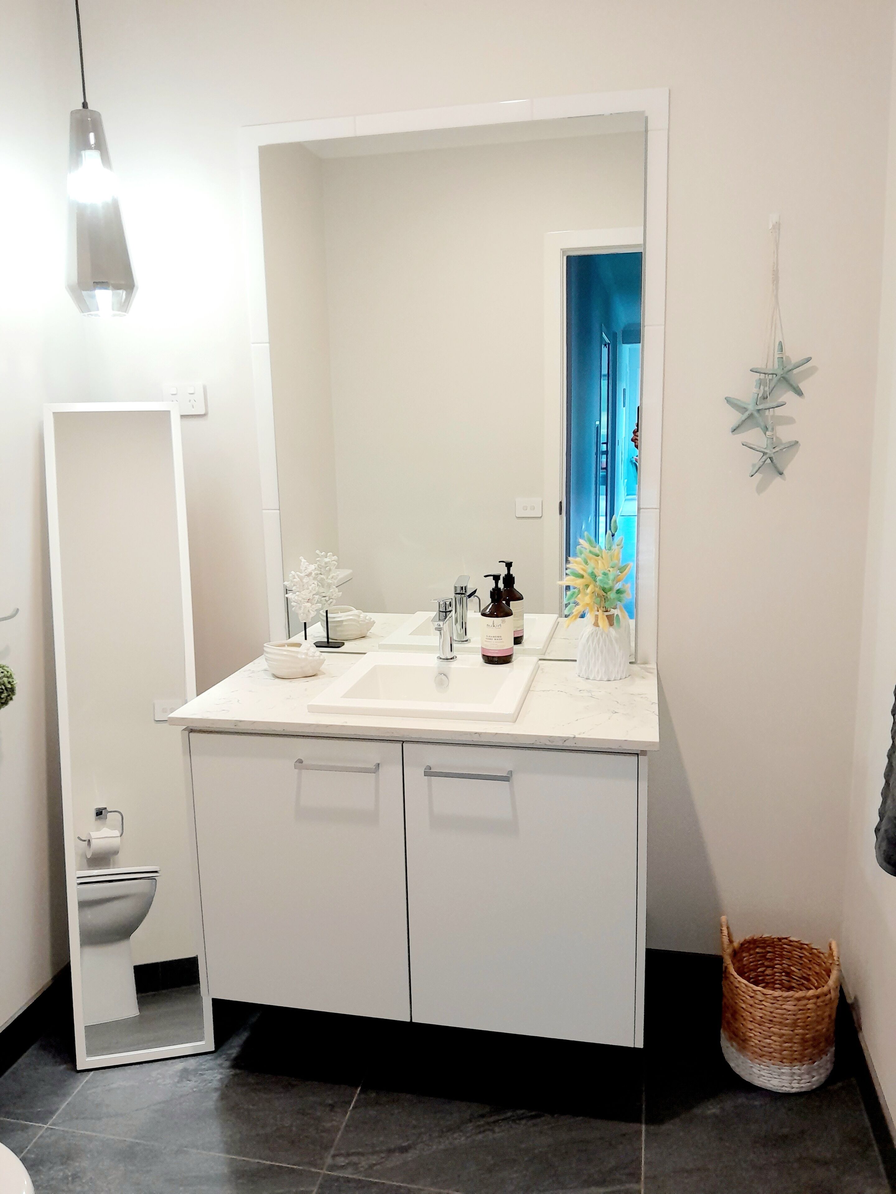 A modern bathroom with a large mirror, white cabinets, a sink, and a small plant.