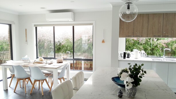 A modern kitchen with a marble countertop, white cabinetry, and a large window overlooking a garden.