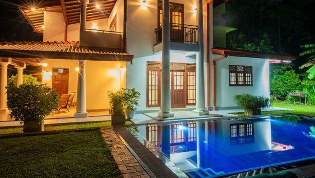 Ein zweistöckiges Haus mit Schwimmbad, Säulen und einem Balkon.