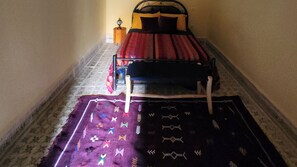 Una habitación pequeña con una cama, una mesita de noche y una alfombra estampada.